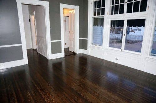 Empty room with dark hardwood floors, gray walls, and large windows for natural light.