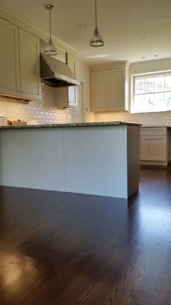 Modern kitchen with white cabinetry, granite island, and polished hardwood floors. Bright natural light.