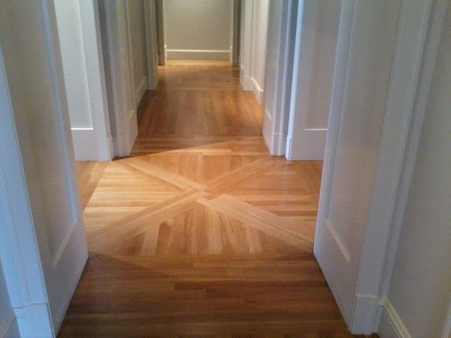 Wooden herringbone patterned hallway floor with white doors and bright lighting.
