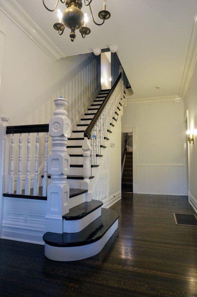 Elegant interior staircase with black and white railings, hardwood floor, and chandelier.