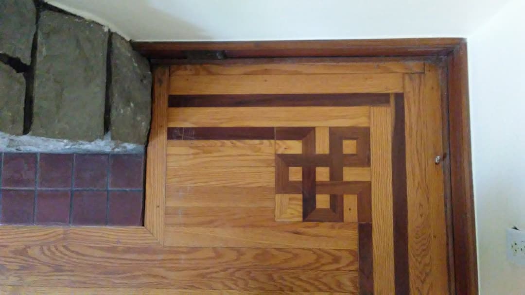 Intricate wooden floor inlay with geometric patterns and stone wall corner detail.