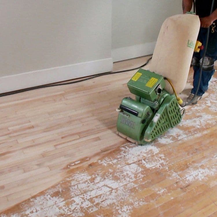 Person using a floor sander on wooden flooring in a home renovation project.