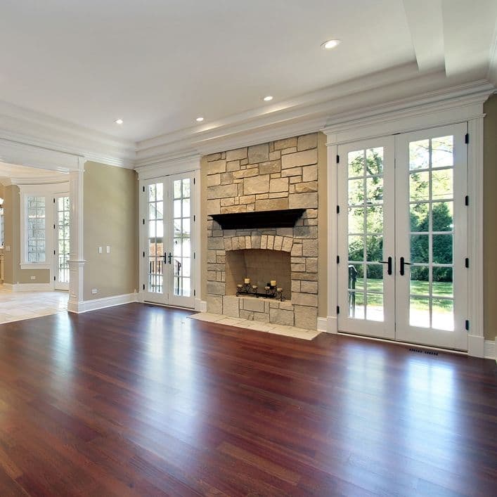 Spacious living room with stone fireplace and large French doors, featuring hardwood floors.