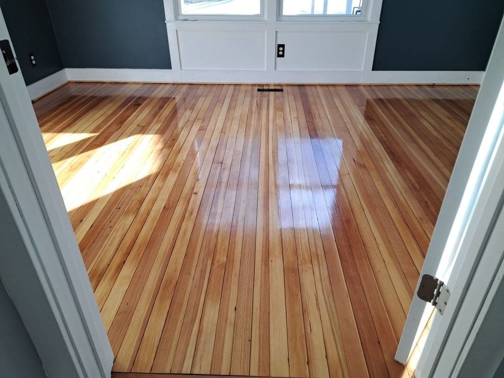 Sunlit room with polished hardwood floor and gray walls, featuring large windows.