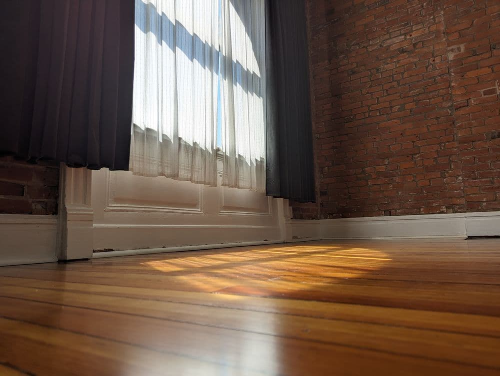 Sunlight streaming through sheer curtains onto a wooden floor in a cozy brick-walled room.