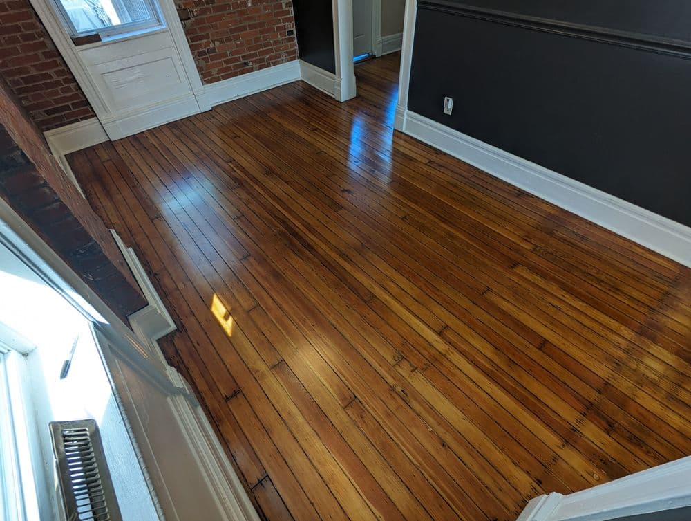 Spacious room with polished hardwood flooring and exposed brick walls, bright natural light.