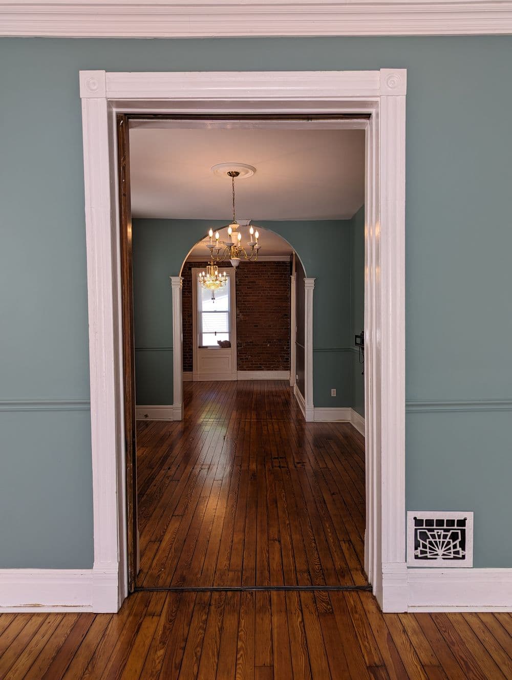 View through an open doorway into a spacious room with hardwood floors and elegant chandelier.
