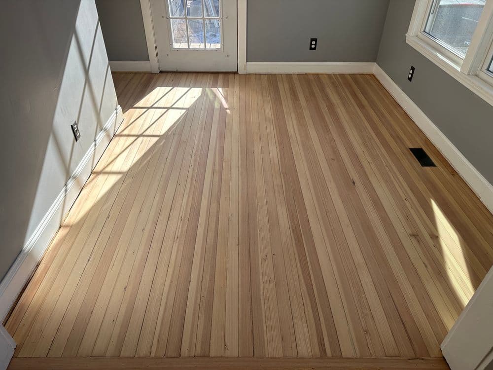Sunlit room featuring polished hardwood flooring with light and dark wood stripes.