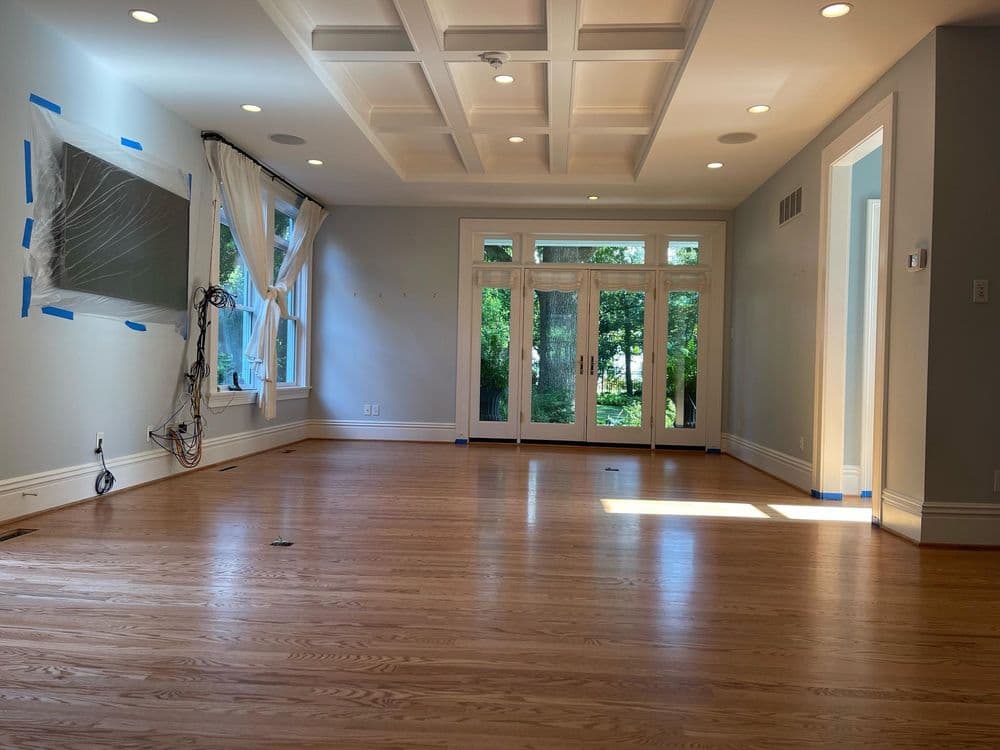 Bright, spacious living room with hardwood floors, large windows, and coffered ceiling design.