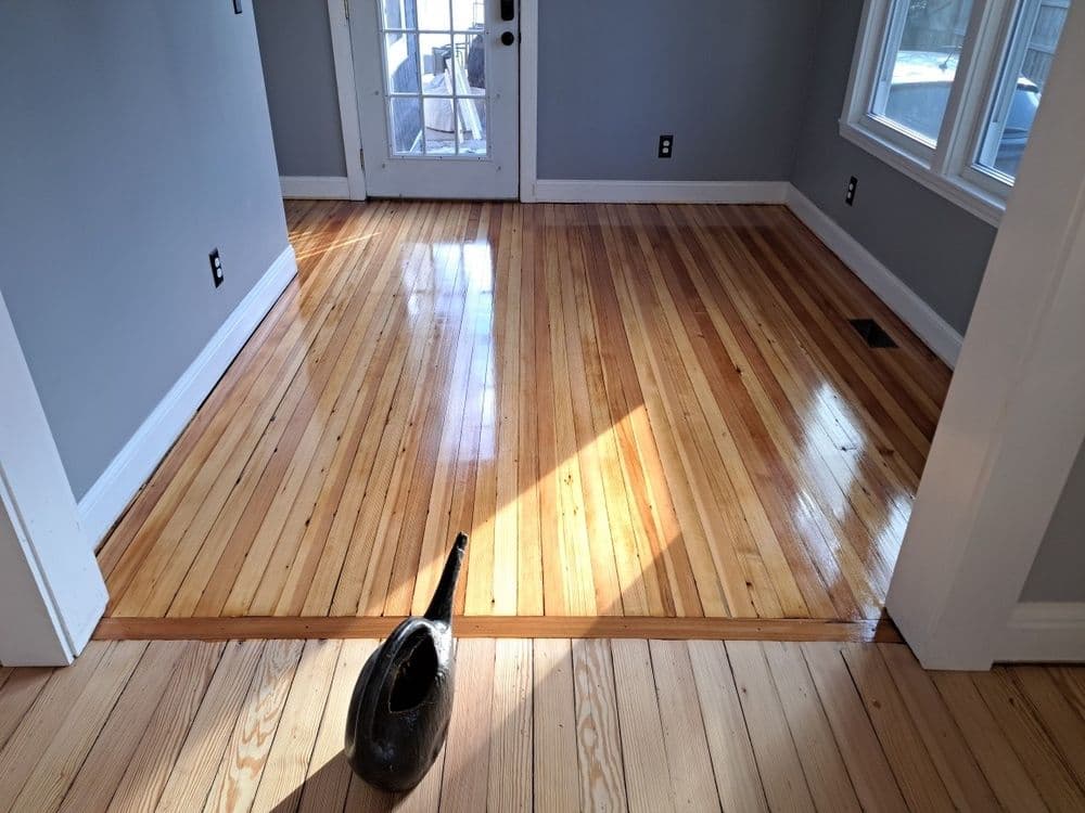 Shiny hardwood floors in a bright room with a black watering can in the foreground.