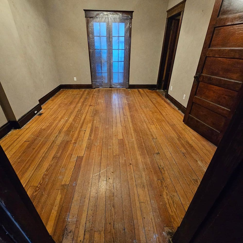 Empty room with hardwood floors and double doors leading to a bright exterior space.
