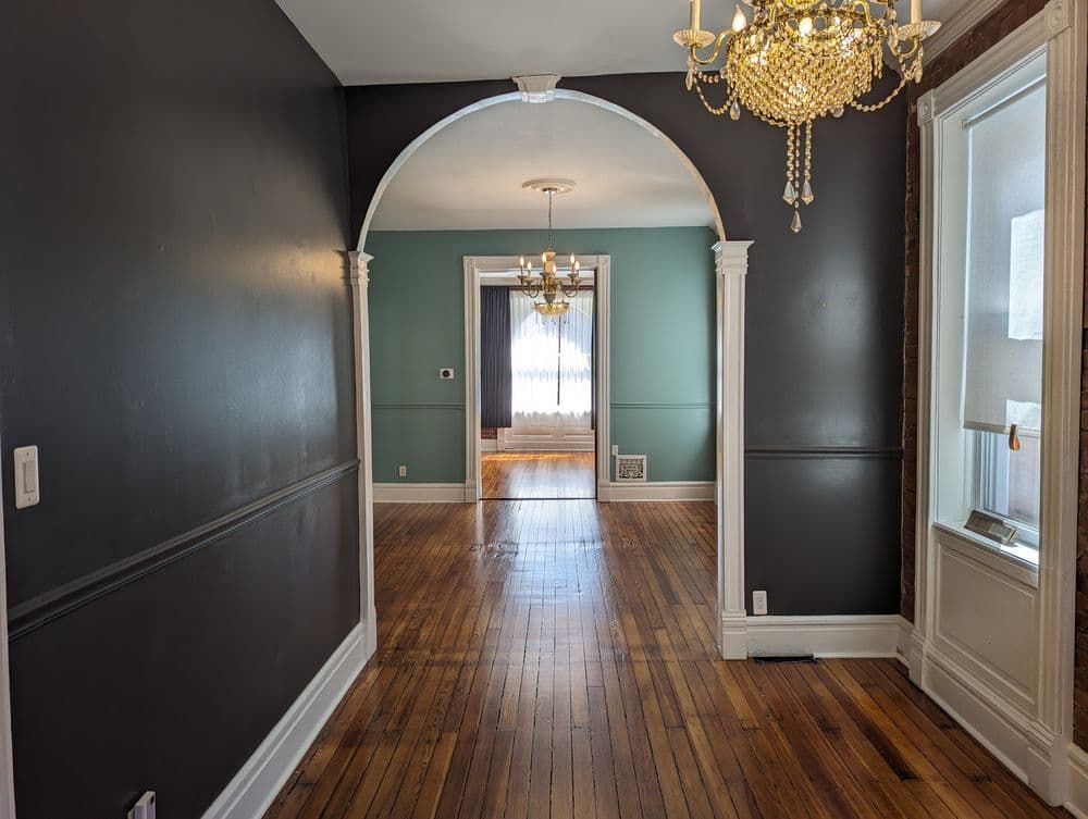 Stylish hallway showcasing dark walls, arched entry, and elegant chandeliers in a vintage home.