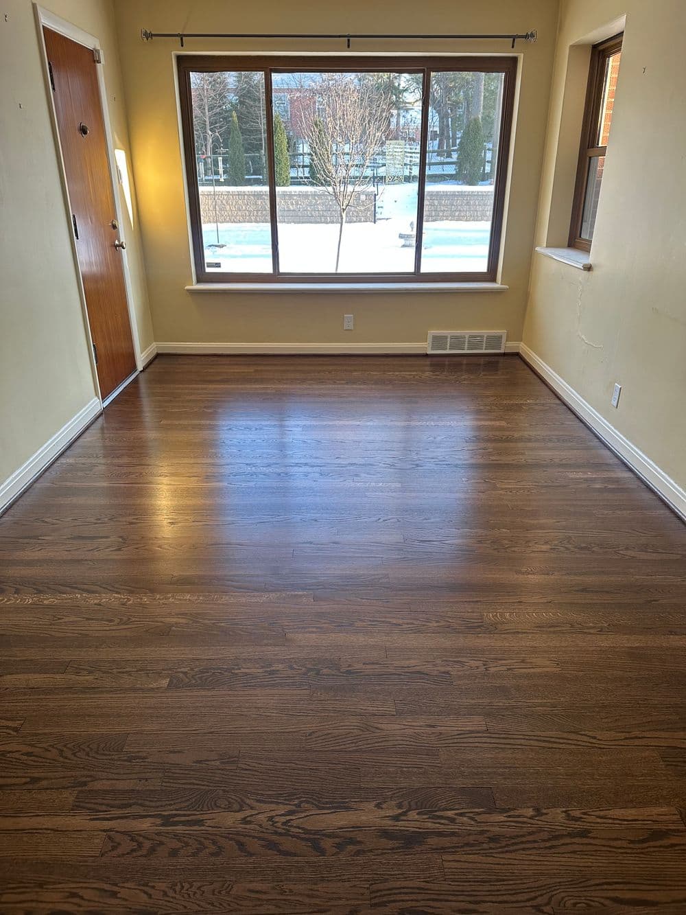 Empty room with hardwood floors and a large window overlooking a snowy outdoor view.