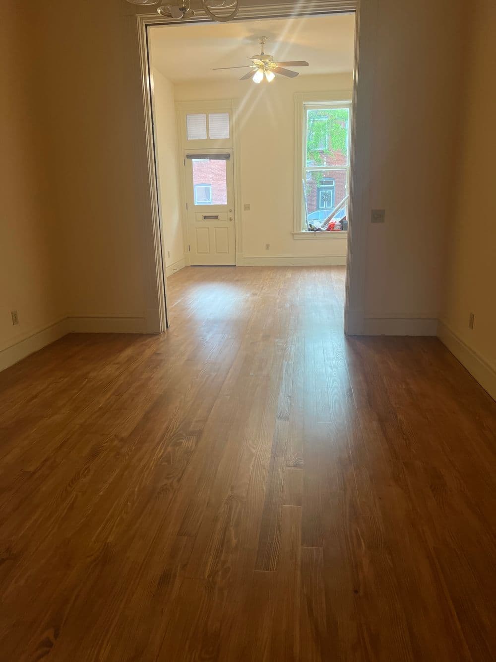 Spacious room with hardwood floors, natural light, and a ceiling fan.