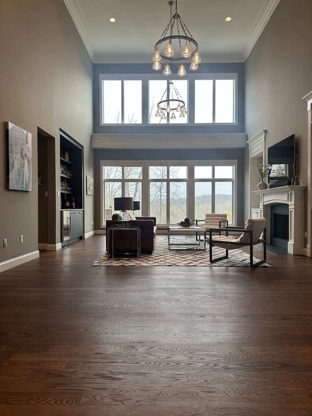 Spacious modern living room with large windows, elegant chandelier, and stylish furnishings.