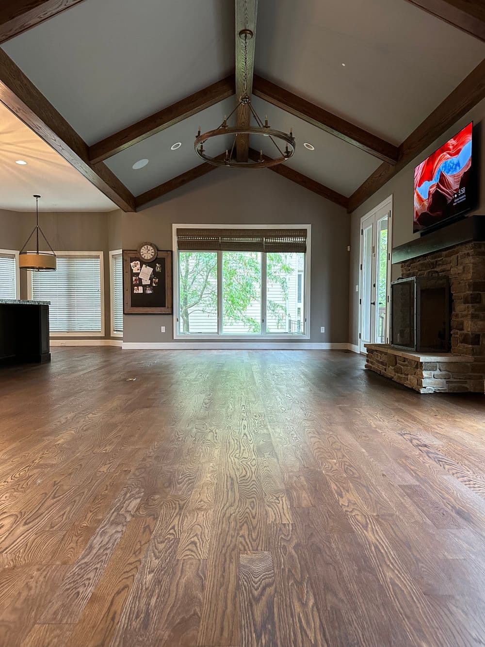 Spacious living room with wooden floors, vaulted ceiling, and large windows for natural light.