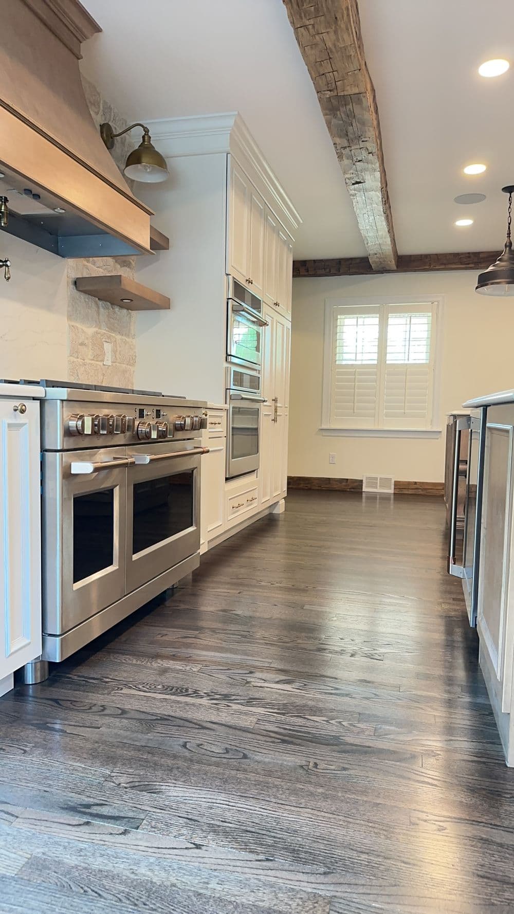 Modern kitchen with stainless steel appliances, wood beams, and dark hardwood flooring.