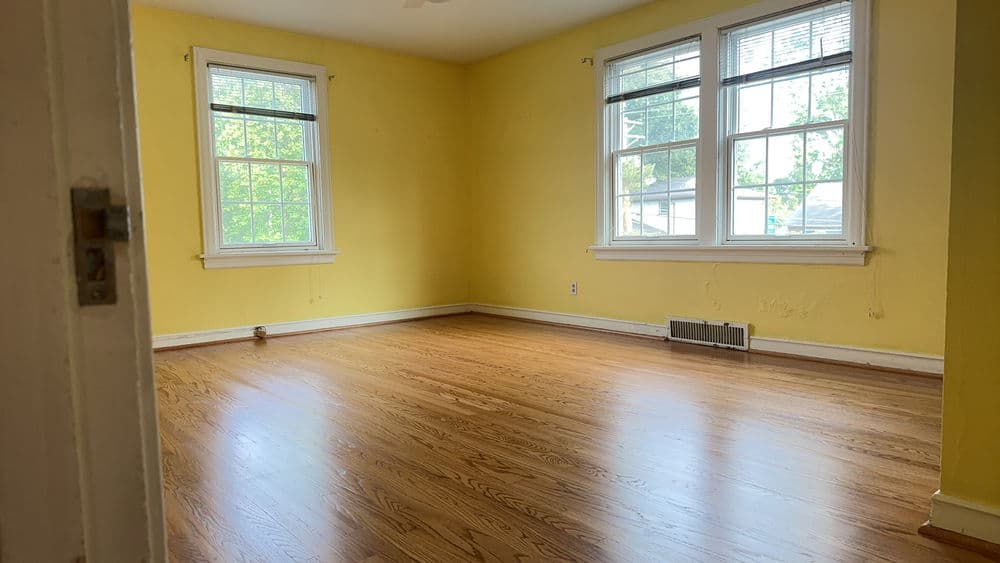 Empty room with yellow walls, wooden floor, and large windows letting in natural light.