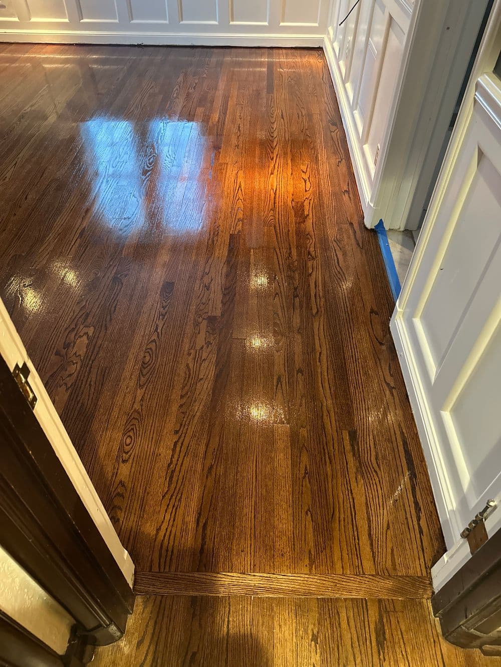 Shiny hardwood floor reflecting light in a modern interior with white paneling.