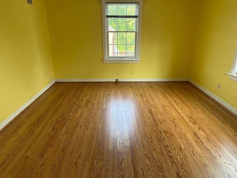 Empty room with yellow walls and hardwood flooring, featuring a window for natural light.