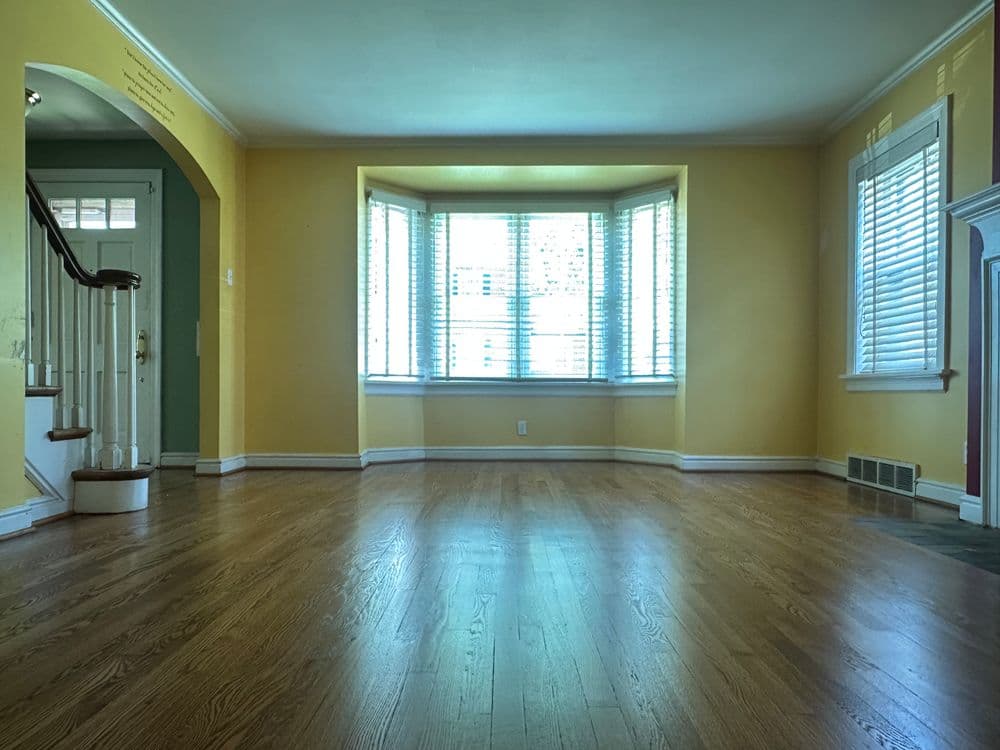 Bright empty living room with yellow walls, hardwood floor, and large bay window.